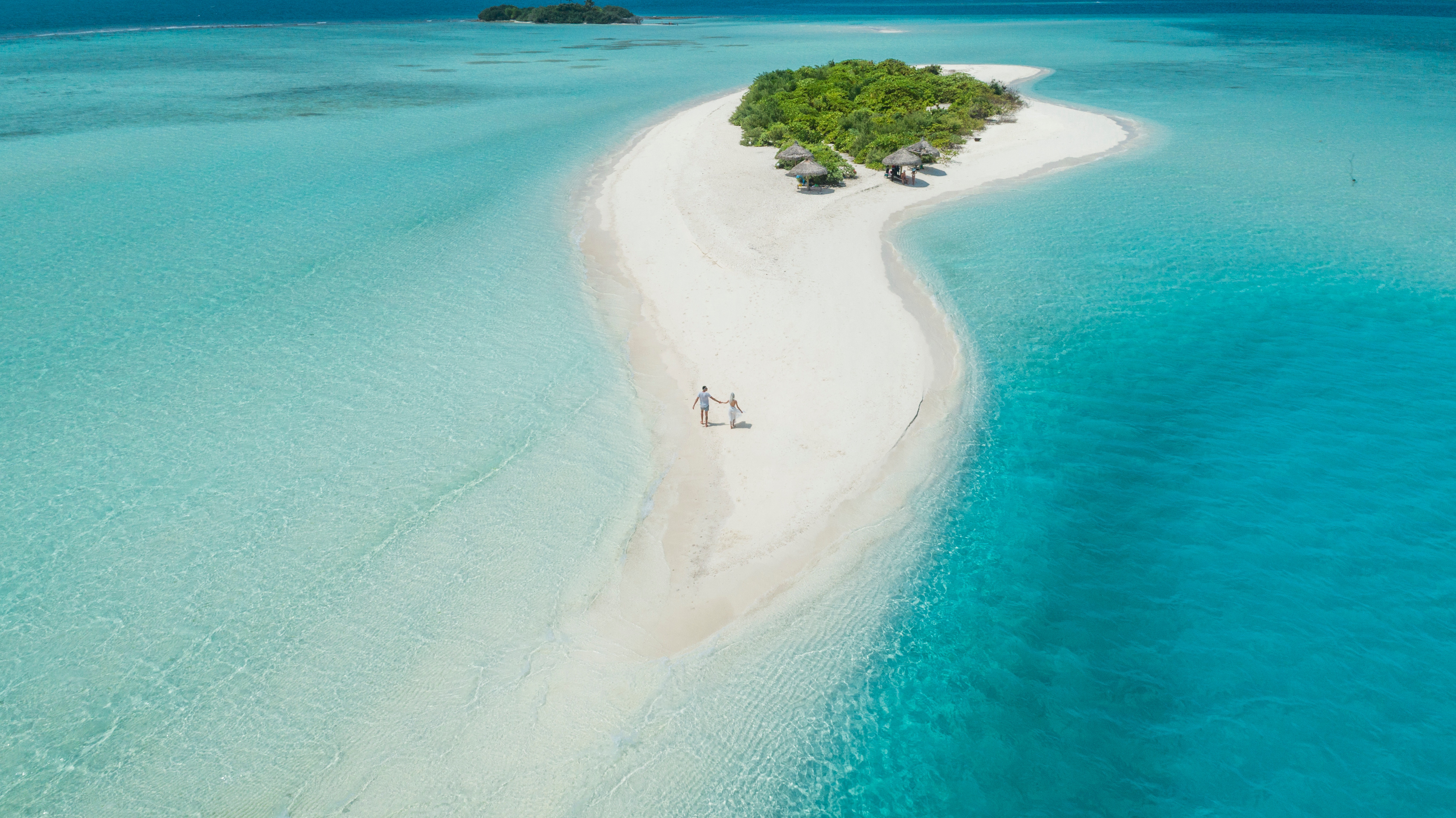 Aerial shot of two people walking on a tiny Caribbean island surrounded by teal water